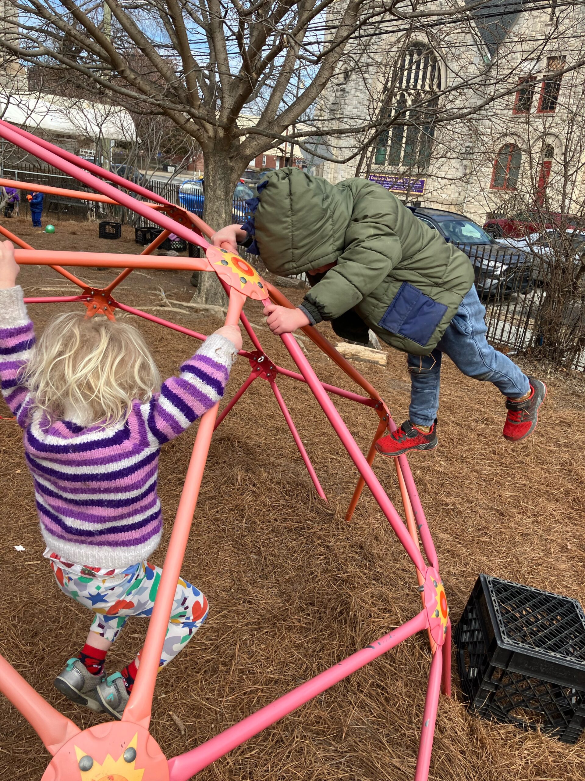 Pre-K kids clamber and hang from the climbing structure in the outdoor play-yard.