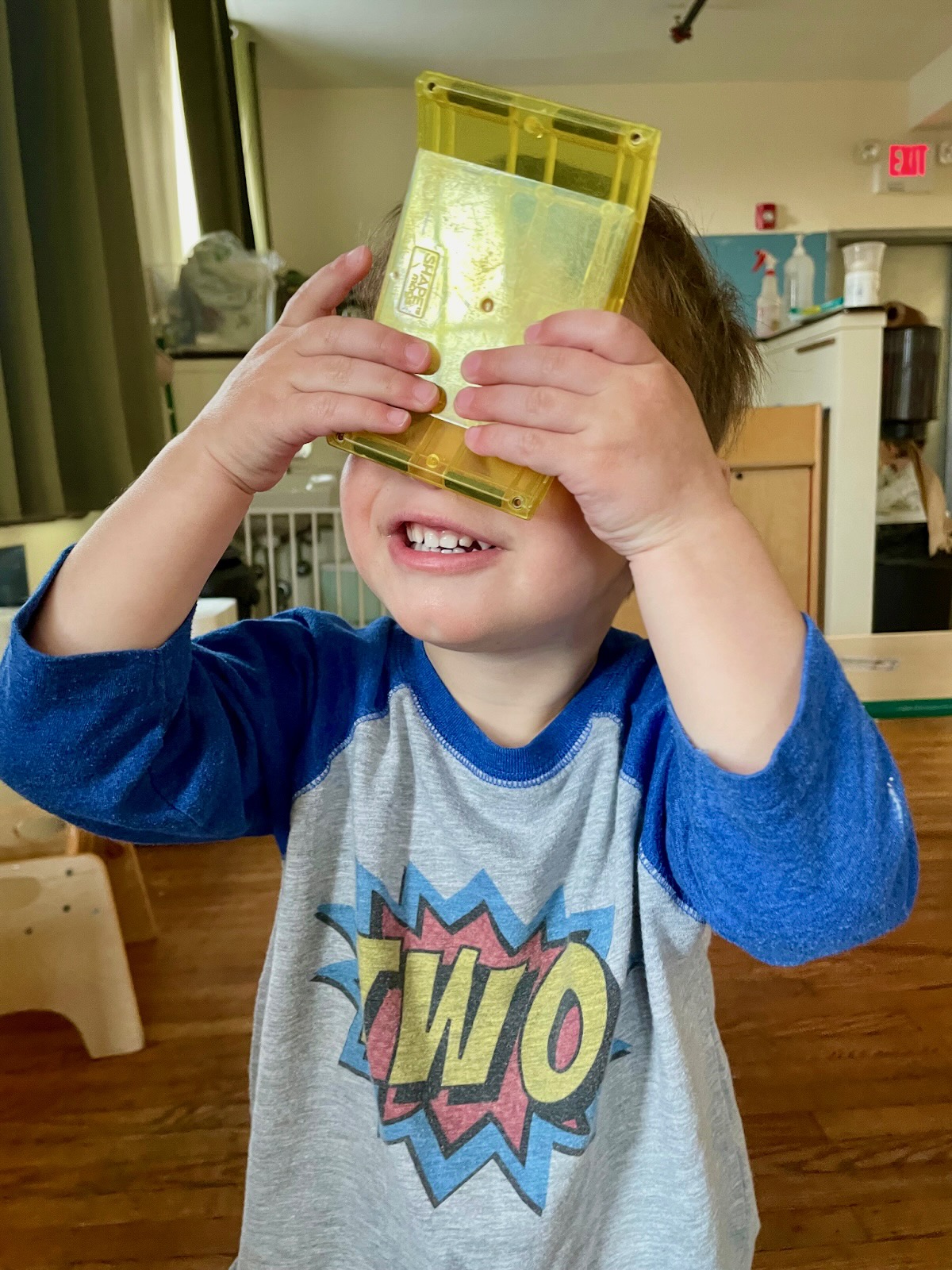 A toddler smiling and holding translucent yellow blocks up to their face to look through.